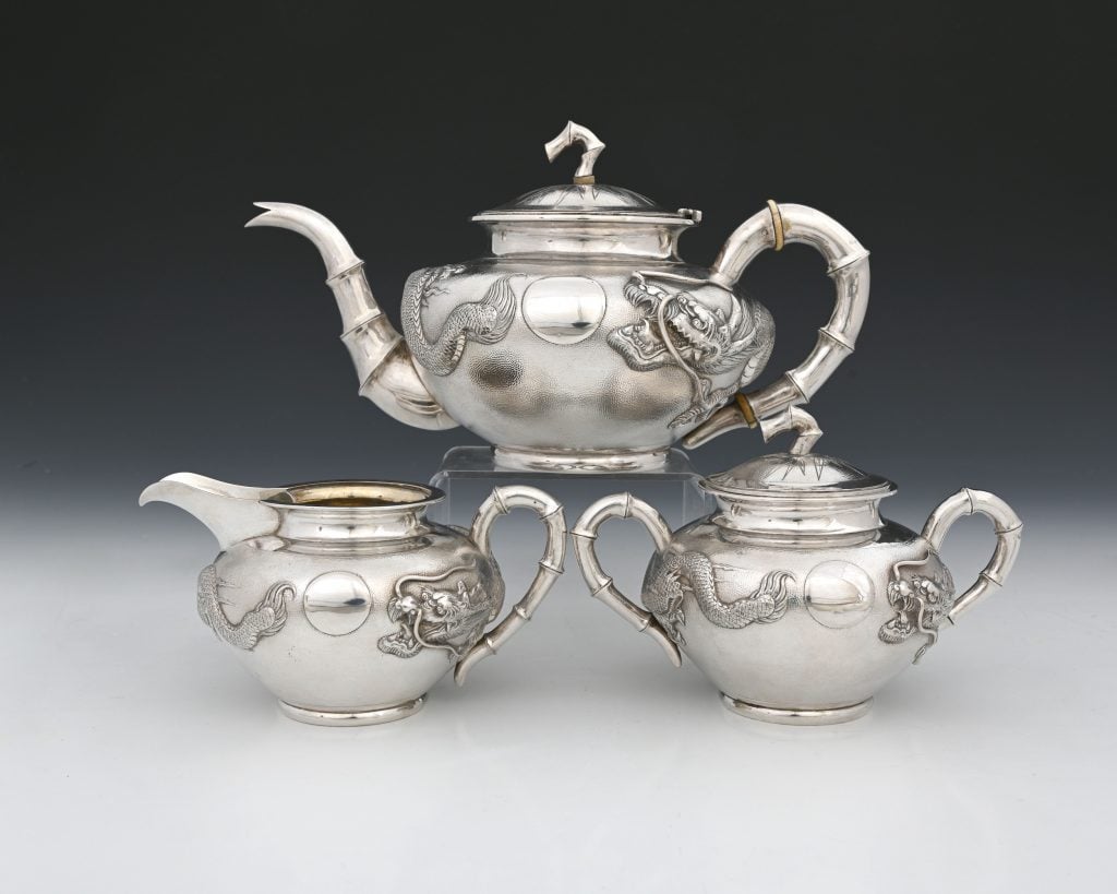 Three silver pots stacked on top of each other against a black background on a grey surface.