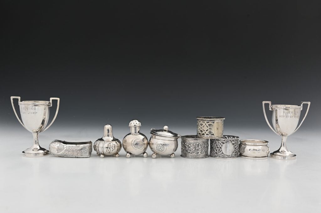 A selection of silver cups and metalware on a grey surface against a black background.