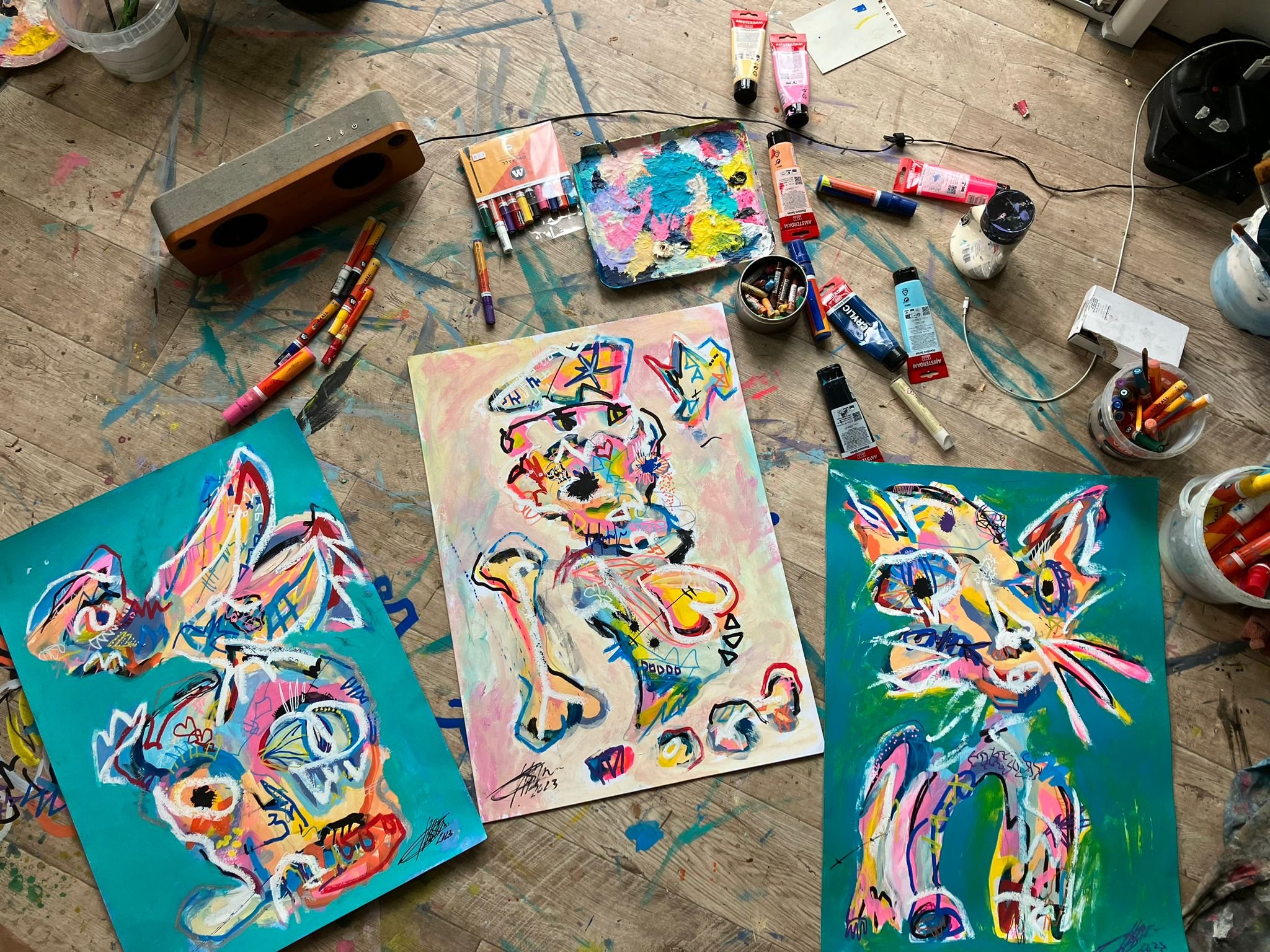 A look on the floor of the studio of Dutch artist Matthijs Scholten, showing three in process works surrounded by various paints, pastels, and other art supplies.