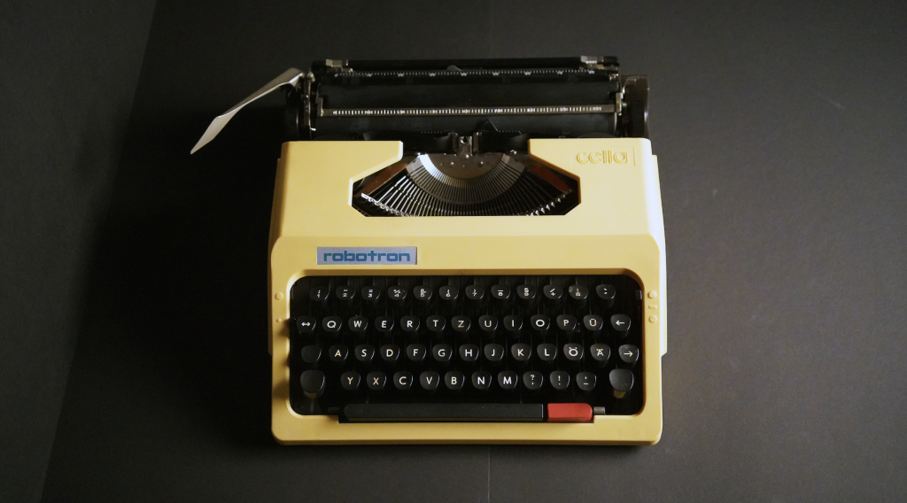 A photograph taken from above of a 1980s-looking yellow typewriter, on a grey background.