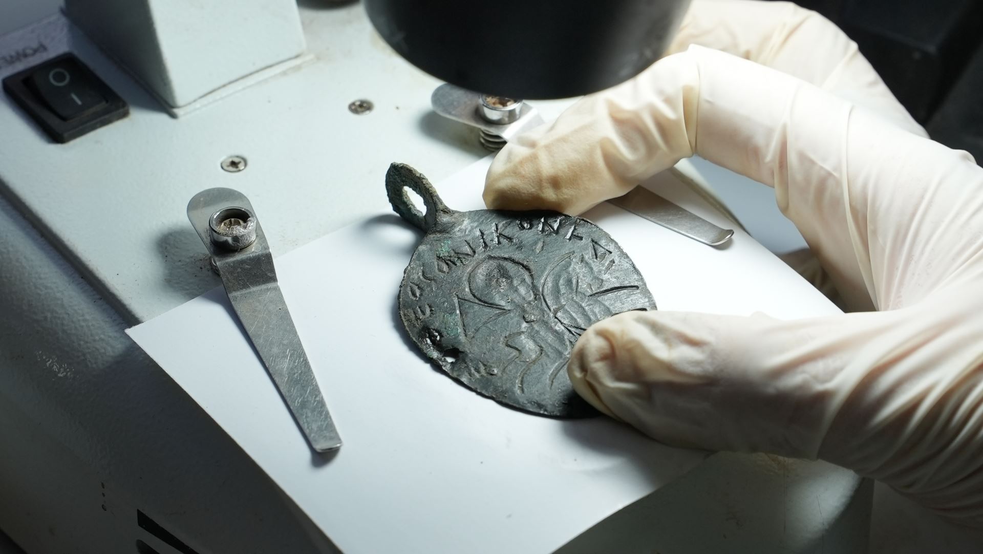 a hand holding a metal amulet on a white table under light