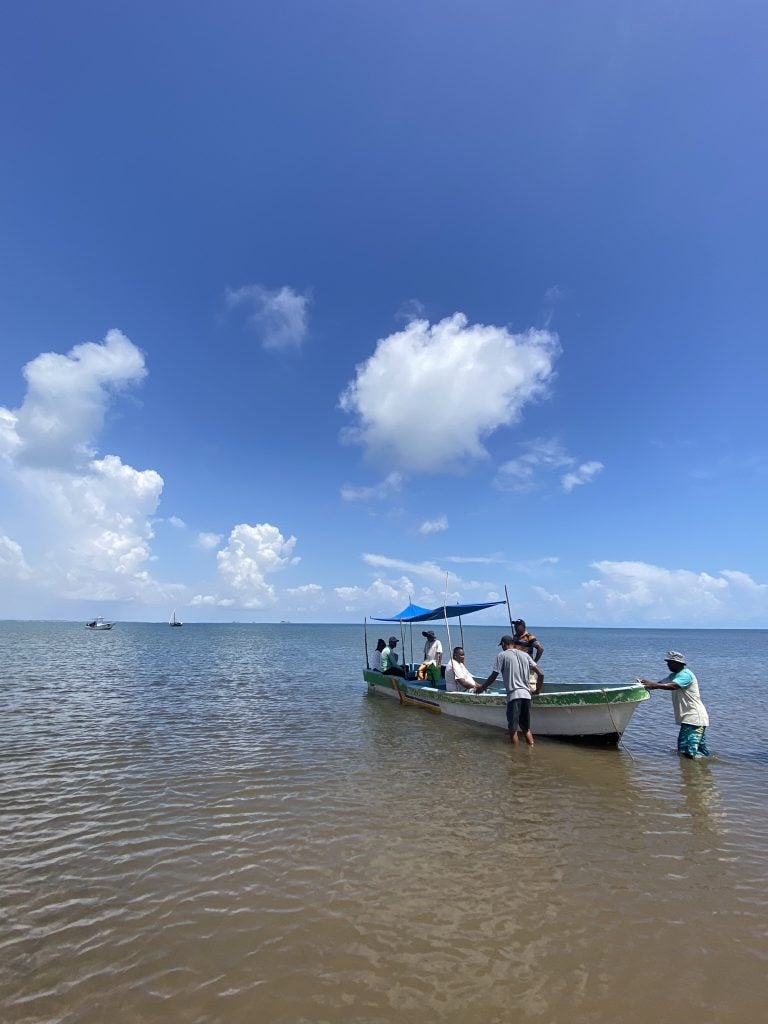 A photograph of shallow waters on the Kenyan coast with several men stood next to and in a small boat.