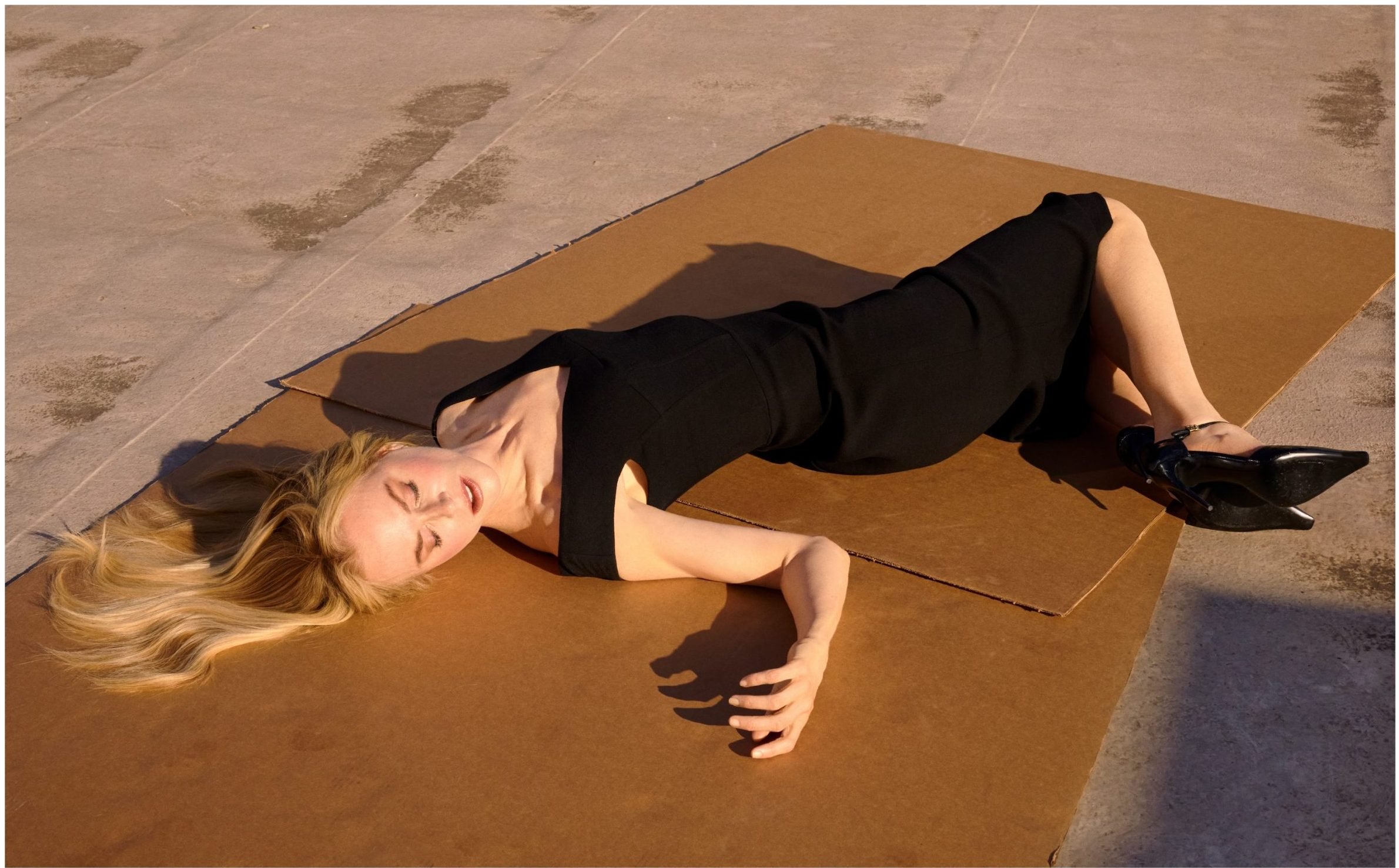 a woman in a black dress lays on pieces of cardboard in sunlight