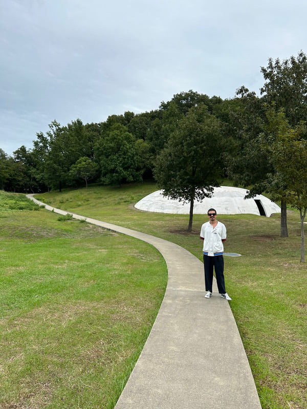 a man in a white shirt and black pants is on a winding sidewalk in an outdoor arts space 