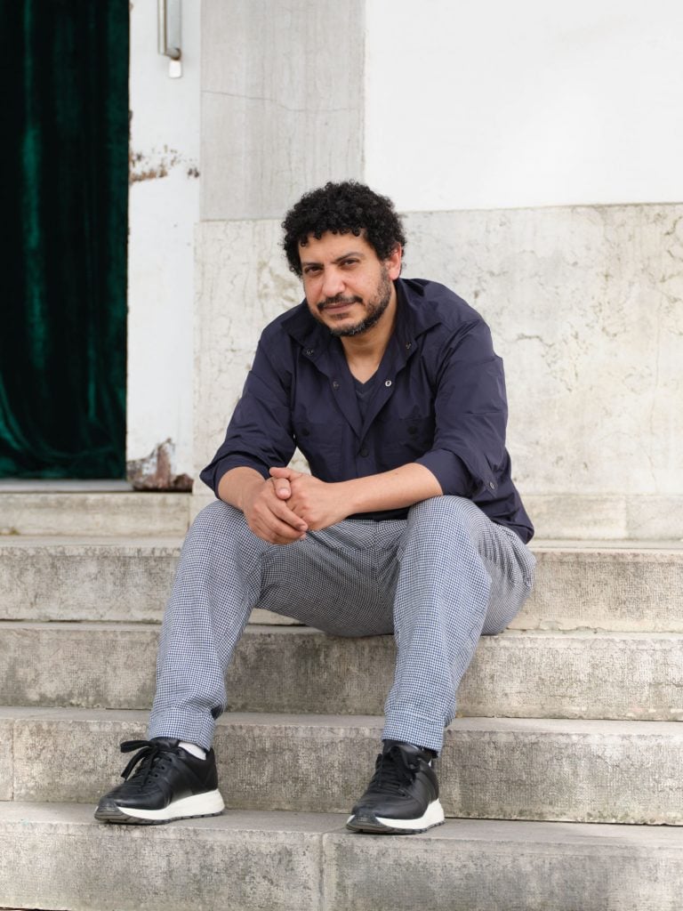 a man in jeans and a black shirt sits outside on cement steps