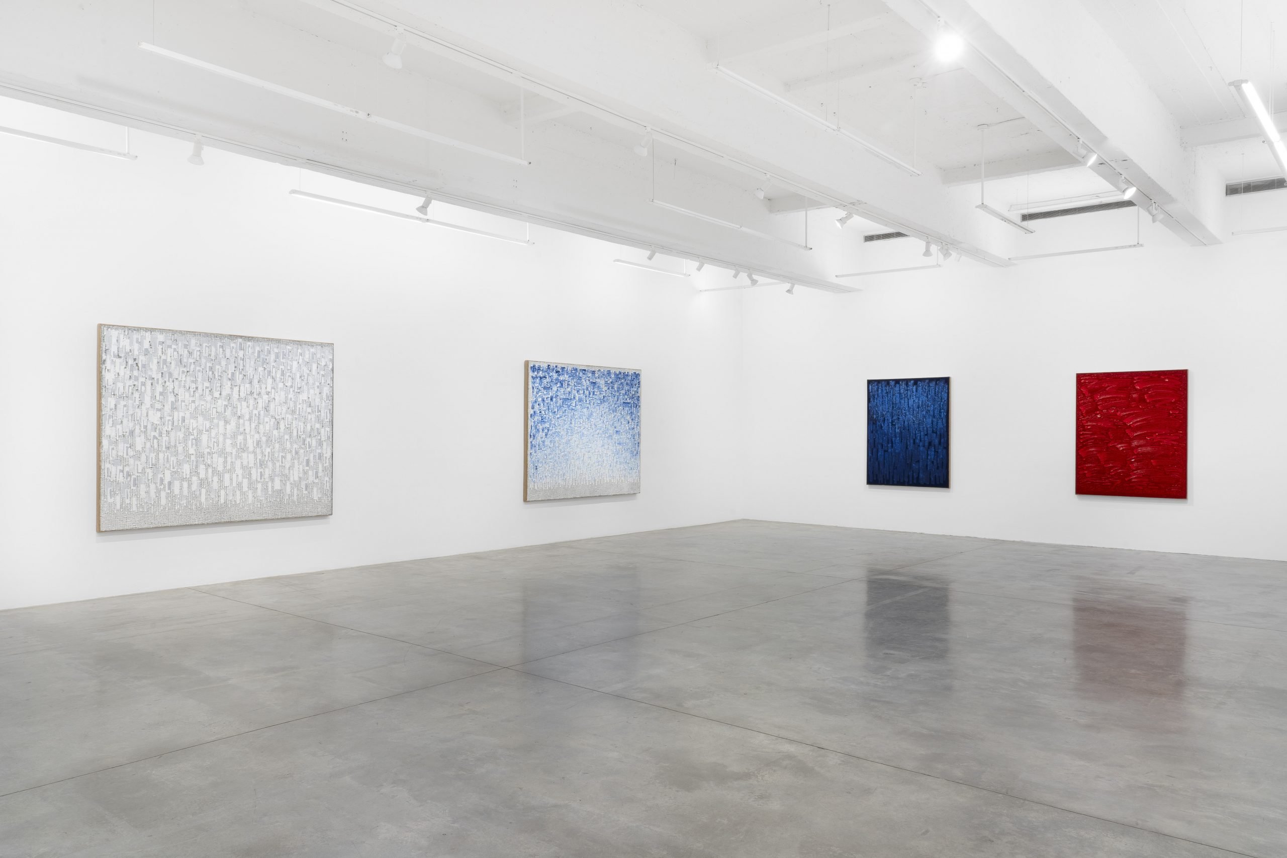 Four paintings in various colors hang in a white-walled gallery