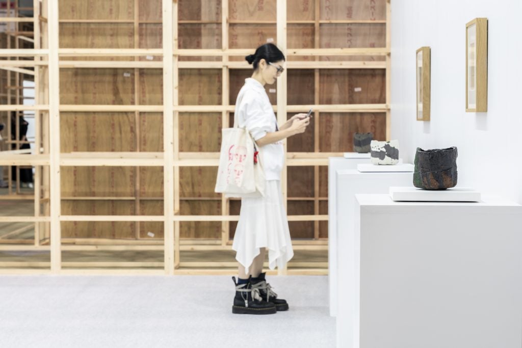 A person in white examines a few ceramics that are sitting on pedestals