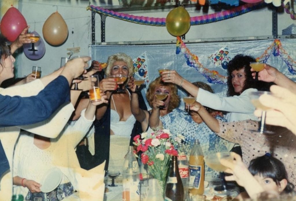 A group of women with glasses raised in a toast, there are balloons and streamers on the wall behind them. 