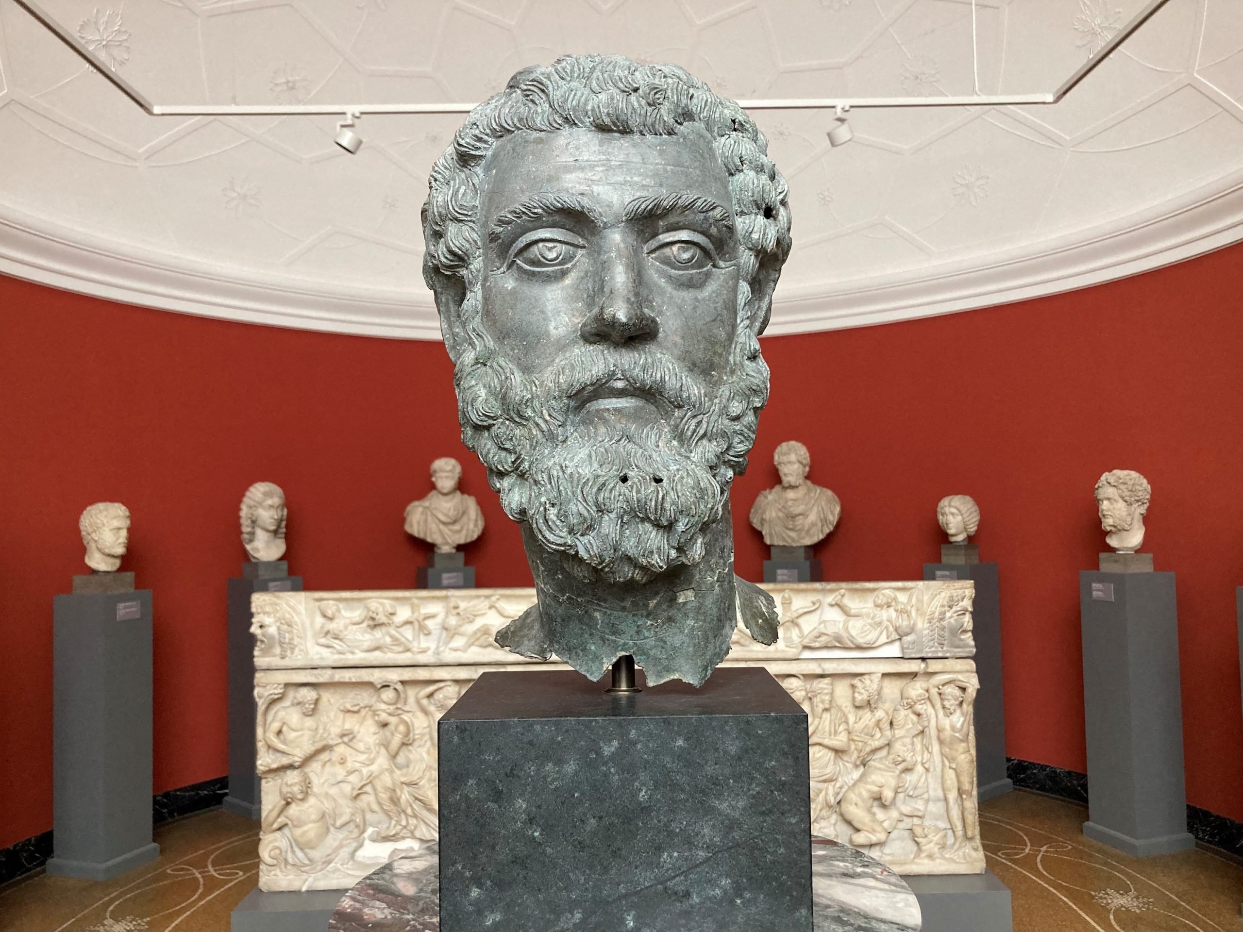 a bronze bust with a row of busts behind and a red wall