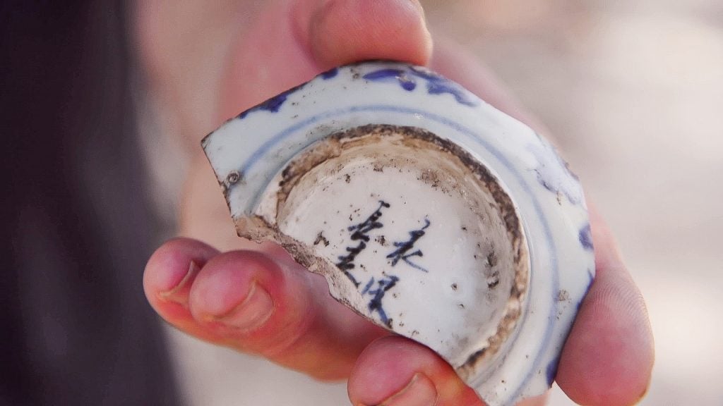 A hand holds a porcelain vase with a Chinese inscription