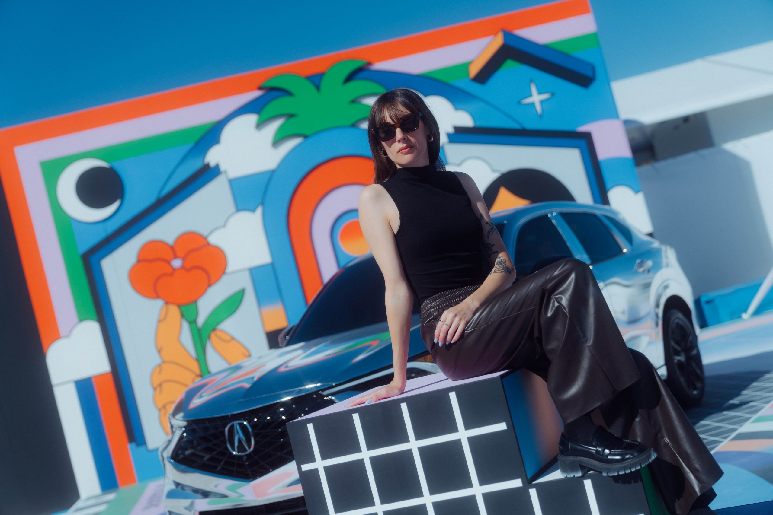 a woman poses in front of a colorful mural in front of a gleaming silver car