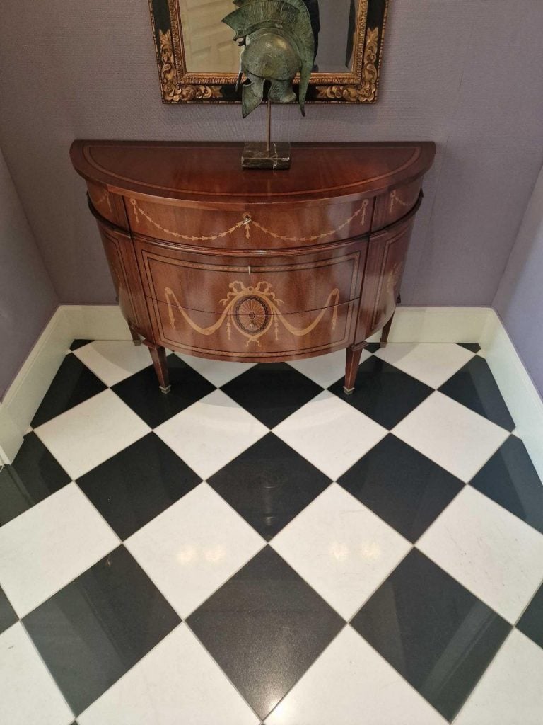 photograph of a small wooden cupboard with a curved design and large drawers underneath a framed photograph on a black and white tiled floor