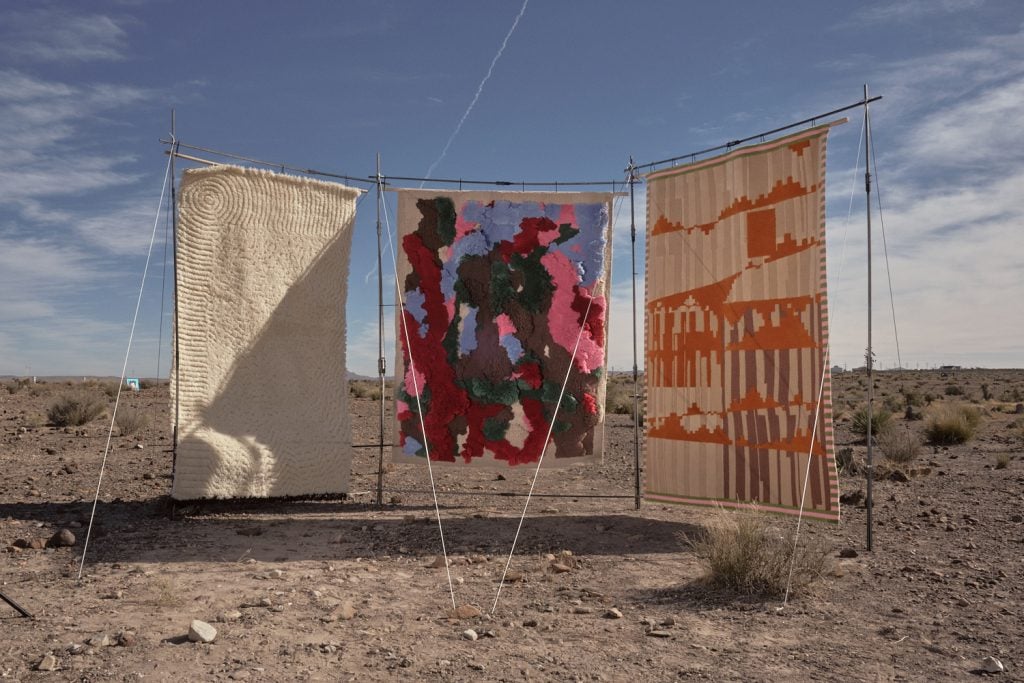 three intricate rugs hang in the desert