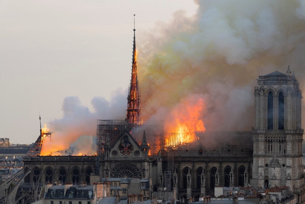 flames and smoke are seen billowing out of notre dame cathedral from afar