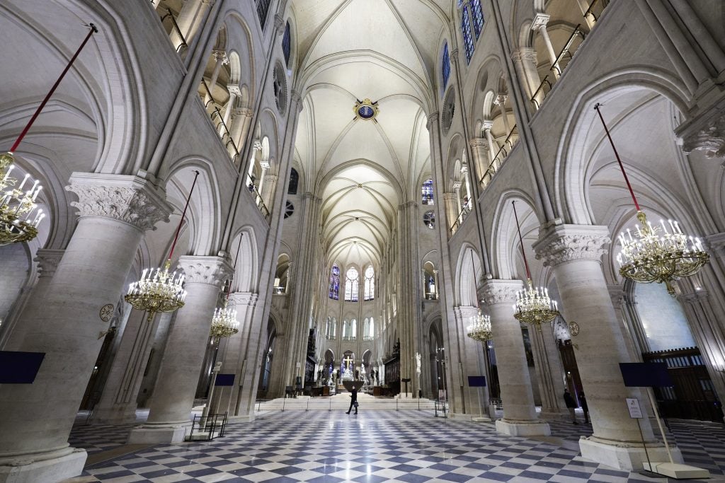 Interior view of Notre-Dame Cathedral, showcasing its grand arches, high vaulted ceilings, ornate chandeliers, and intricate architecture, emphasizing its Gothic design.