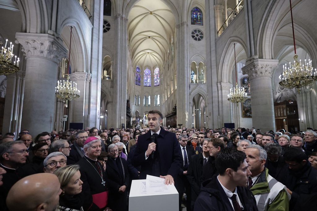 a man in a suit speaks into a microphone in front of a large crowd inside a church