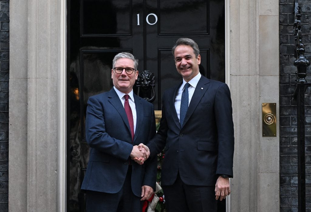 Two suited men shake hands outside the iconic black door of 10 Downing Street, showcasing a formal meeting at a notable political location.