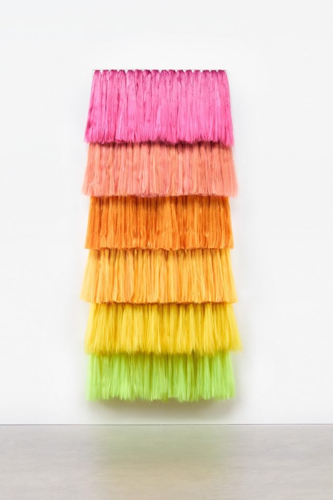 a modern art piece has pink yellow orange and green cascading synthetic hair 