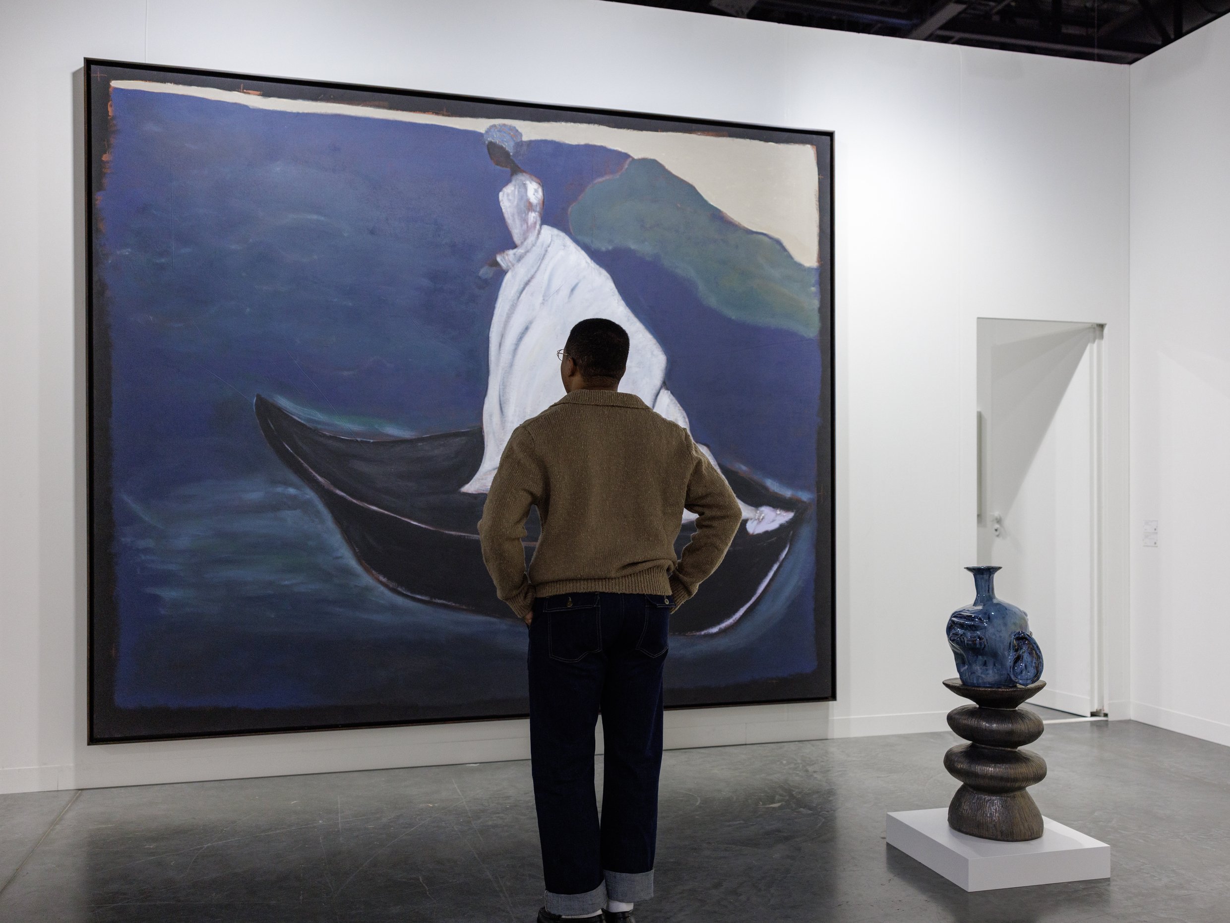 A large painting hangs on a white wall. A man is viewing it.