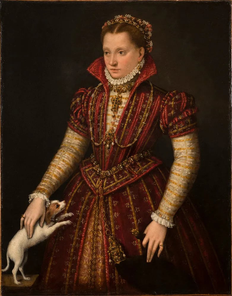 Lavinia Fontana, Marriage Portrait of a Bolognese Noblewoman. An Italian Mannerist Old Master painting of a young woman in an ornate red gown with a ruffled collar, gold jewelry, and flowers braided into her hair. A small dog is jumping up she can pet it. 