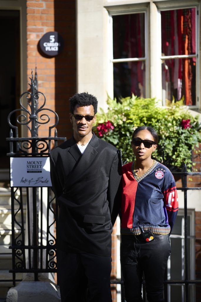 A man and a woman posing in sunglasses outdoors in front of a home