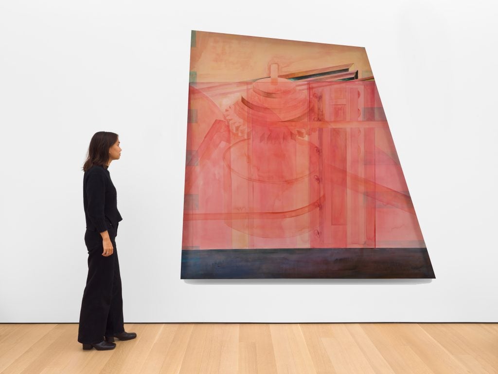 a woman stands next to a geometrically shaped painting of a machine 