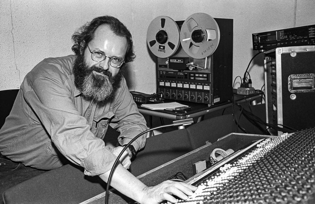 Black and white photo of American composer Phill Niblock as he poses at a mixing desk during a sound-check before a concert of his works in the World Music Institute's 'Interpretations' series at Merkin Concert Hall, New York, New York, January 17, 1991. 