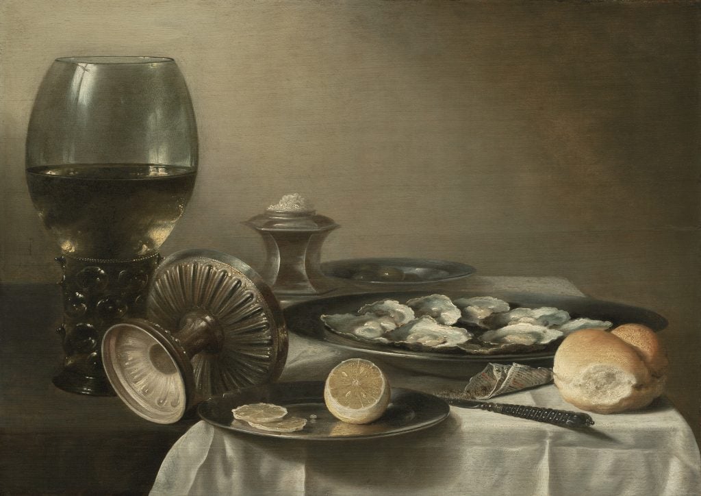 A still life painting showing a table set with a glass of wine, a dish of oysters, a loaf of bread, a half-sliced lemon, and a decorative salt cellar. The composition highlights the textures and reflections of the various items on the table.