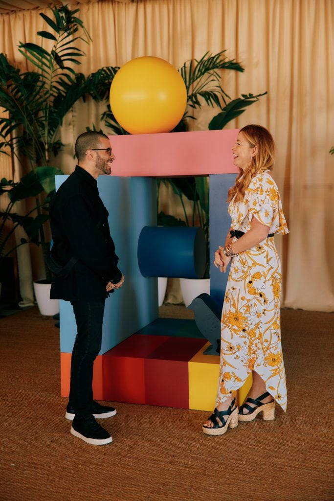 Kate Bryan chatting with artist Typoe beside a colorful geometric art installation at an event.