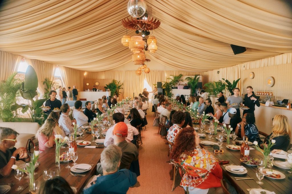 A bustling gathering at a luxurious, tented dining area with natural light and vibrant decor.