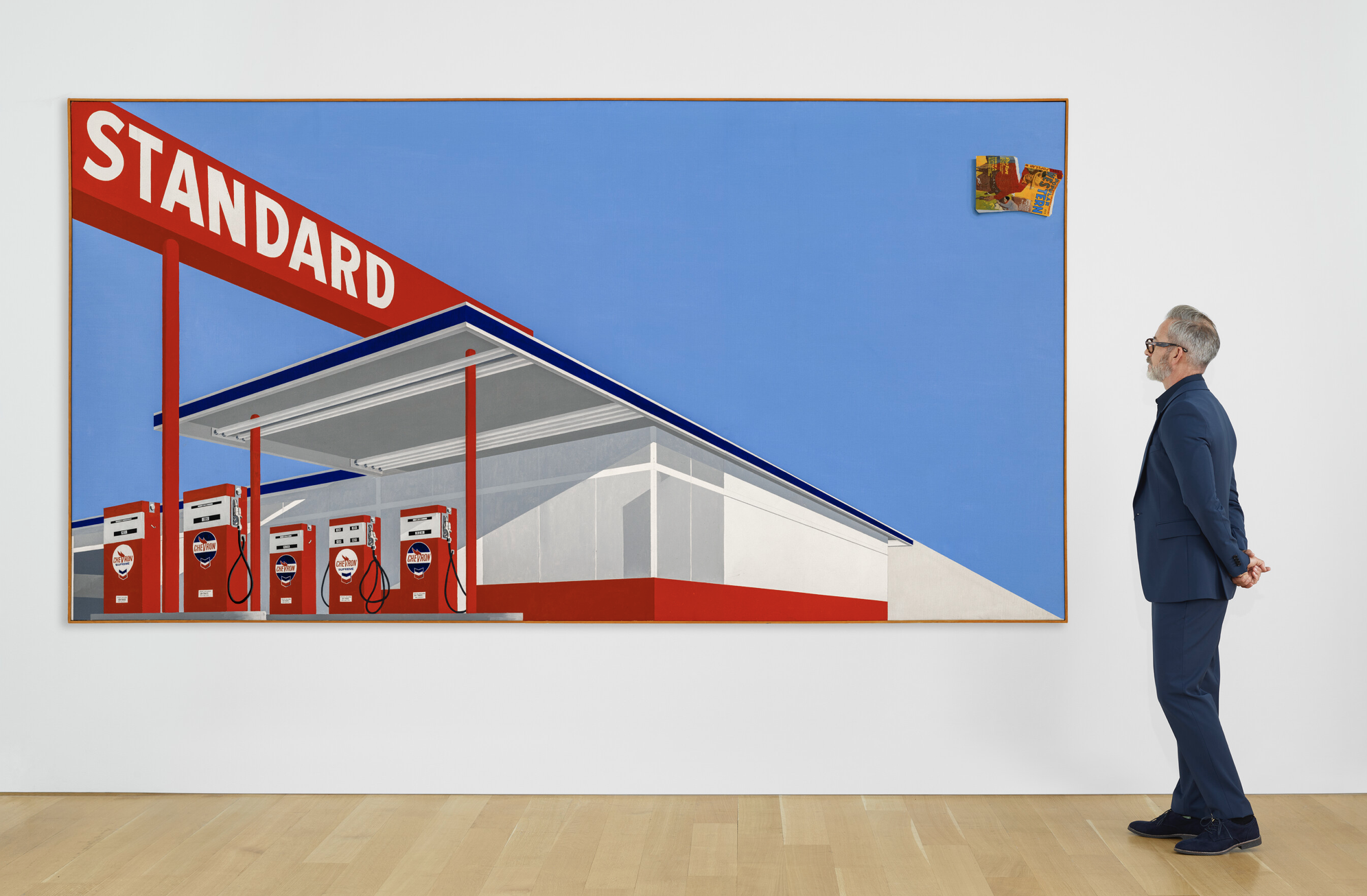 A man stands near a painting of a gas station