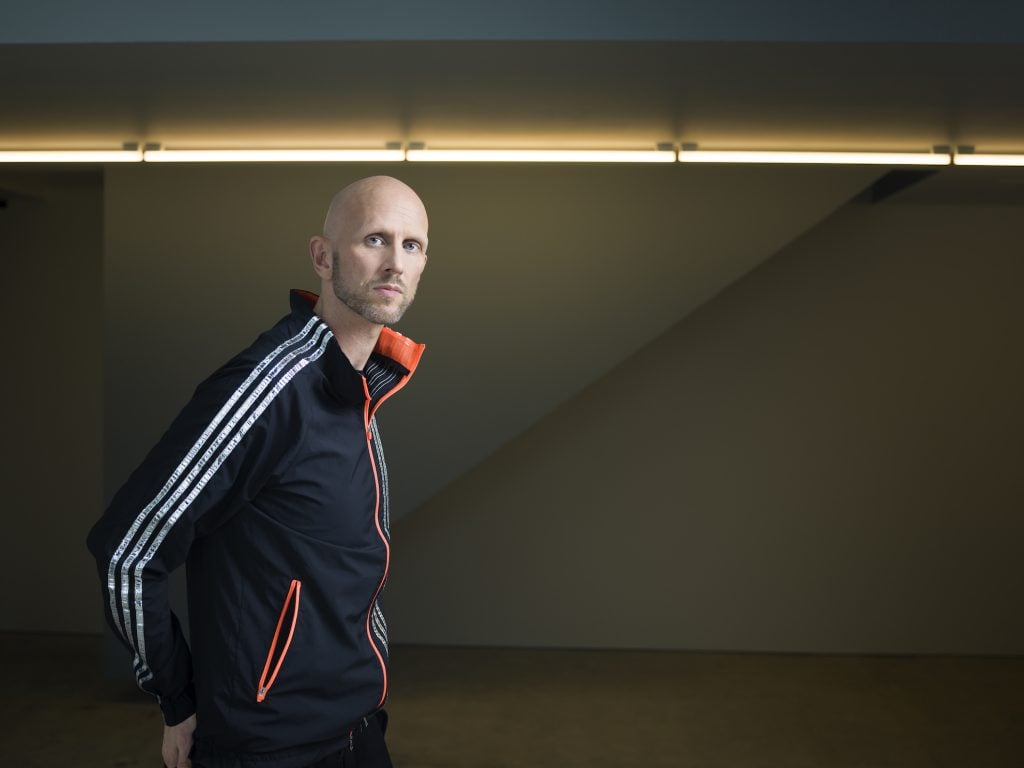 Wayne macgregor in a tracksuit with white stripes, against a dark background