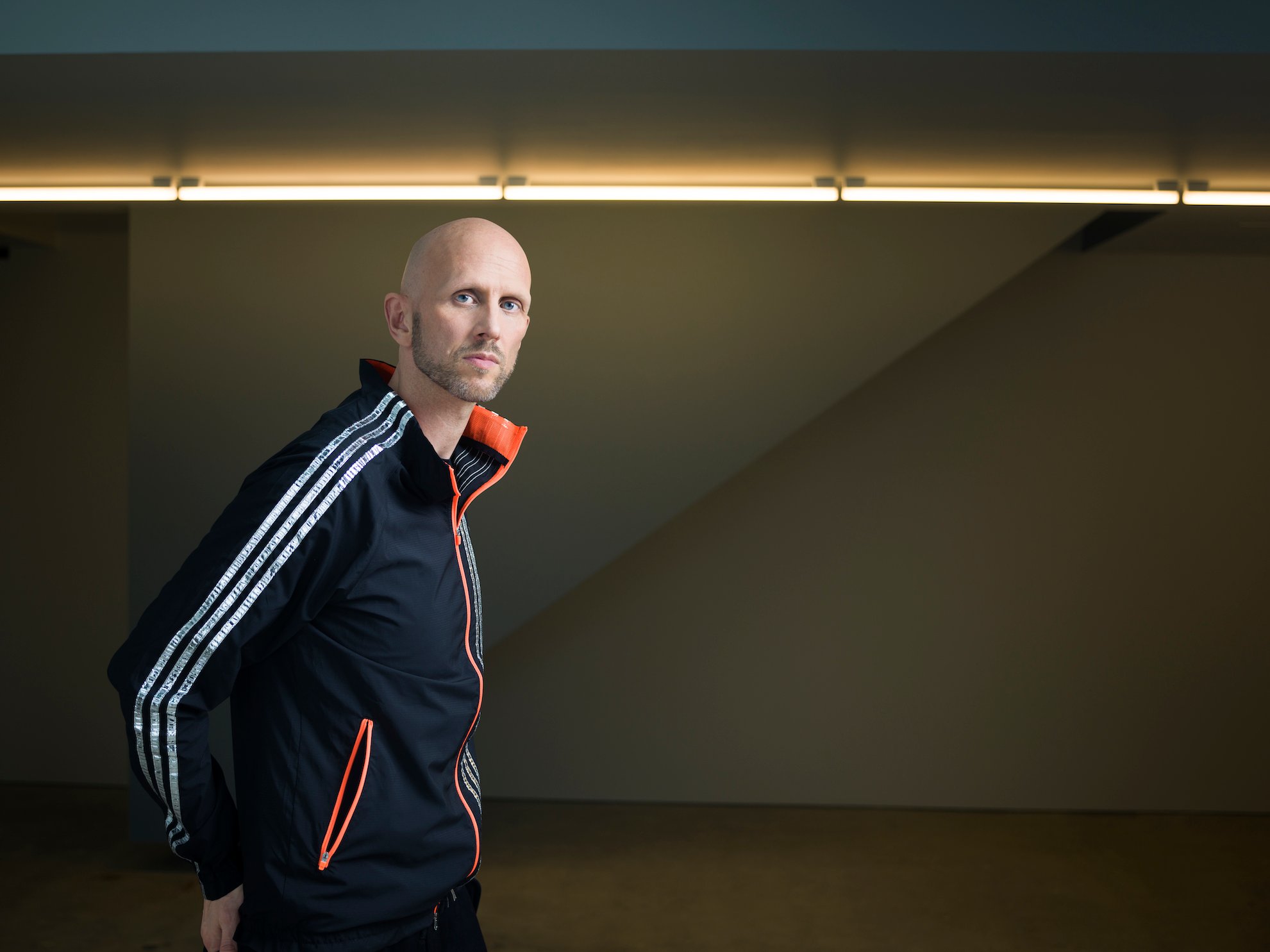 Wayne macgregor in a tracksuit with white stripes, against a dark background