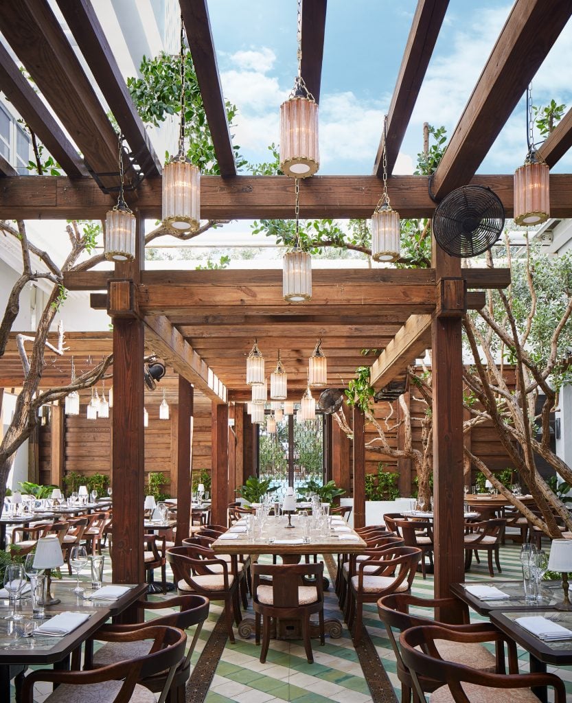 An elegant outdoor dining area with wood pergolas, greenery, and lantern-style lighting at Cecconi’s.