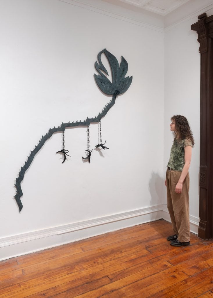 "Helen Evans Ramsaran: Strange Fruit," installation view, with Stranglehold, a leaf-like form with lynched figures hanging from it. A white woman with curly hair is looking at the work.