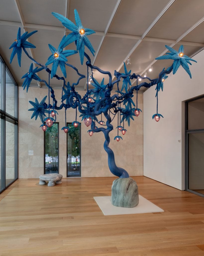 a sculpture of a tree has dangling glass strawberries 