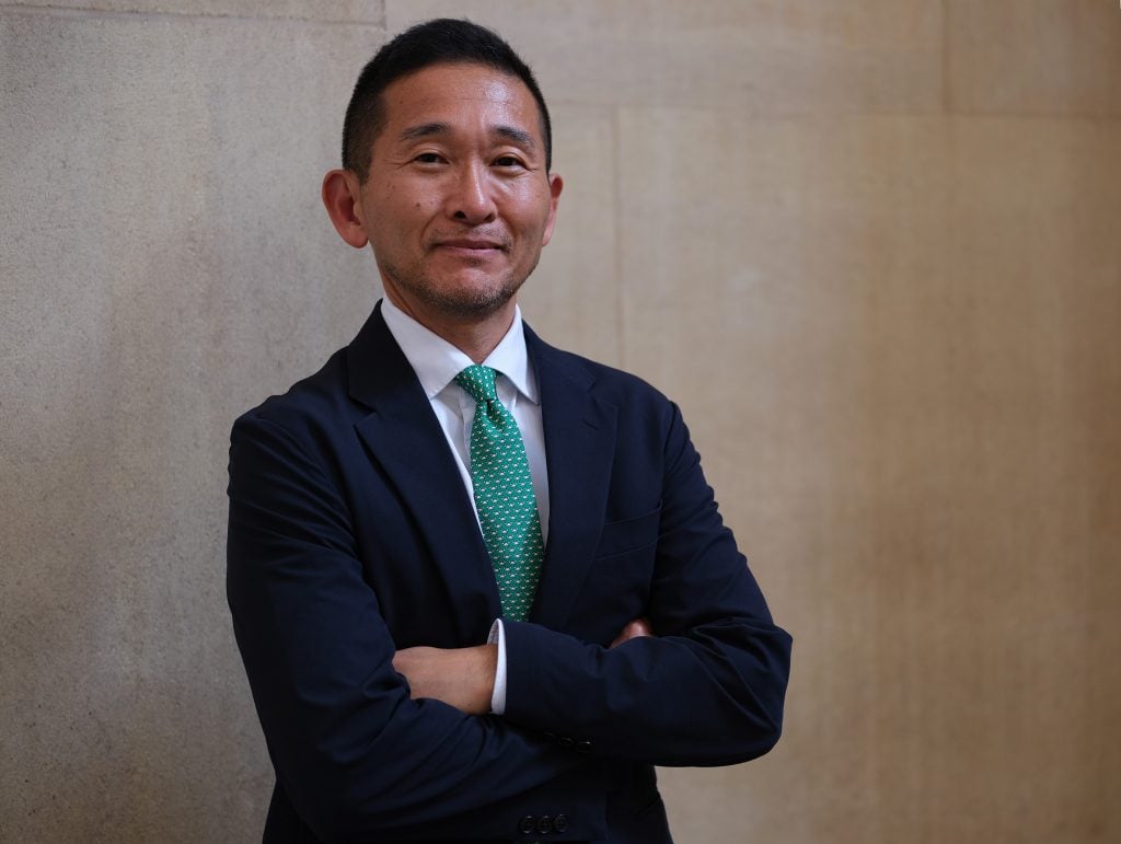 An Asian man with dark hair dressed in black suit jacket, white shirt, and a tie in turquoise