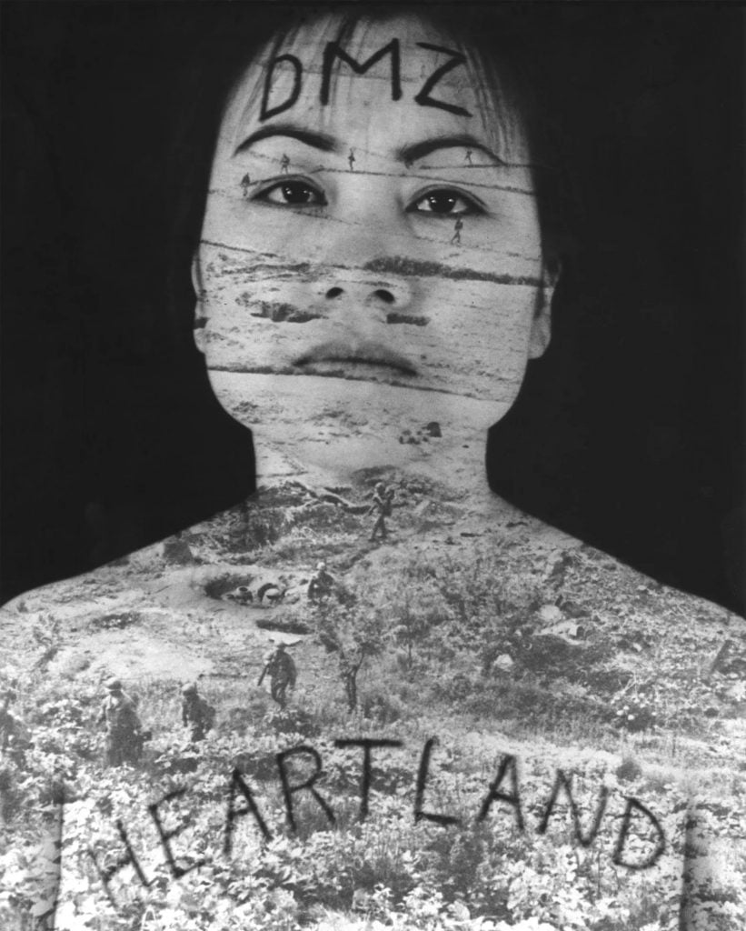 Yong Soon Min, “Defining Moments No. 2” (1992). A black and white photo of a young Asian woman with 'DMZ' written on her forehead and 'Heartland' on her chest in black. The background is black, and she is seen from the collarbone up, skin bear. A double exposure shows the barbed wire of Korea's demilitarized zone, with soldiers moving through the landscape. 