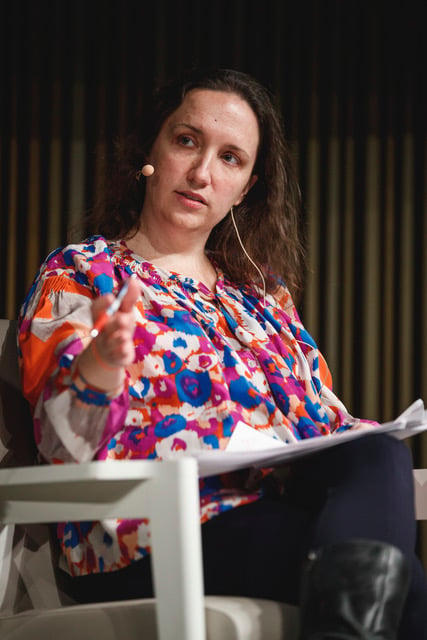 Photo of Gagosian Chief Creative Officer Alison McDonald in a bright patterned blouse and an ear mic speaking at a conference. 