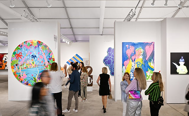 Inside the booths section at art miami 2023 with large-scale colorful art on the walls and visitors milling about.