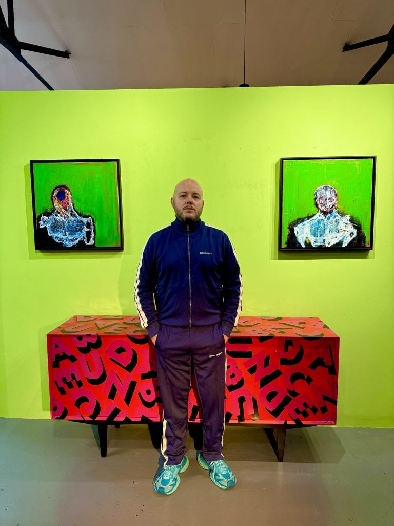 Artist Lincoln Townley in front of the diptych work inspired by Francis Bacon and in front of a red cabinet with black caligraphy.