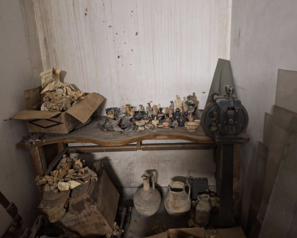 A photograph depicting a desk in a dingy Athens basement crowded with stolen Ancient Greek artifacts.