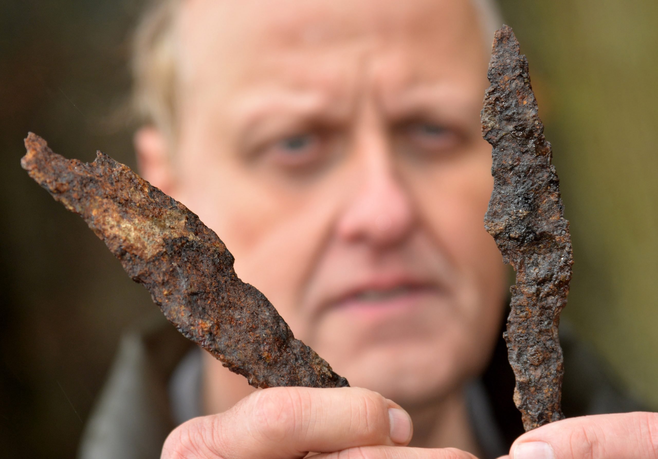 photograph of a middle aged man holding two rusty spearheads in his hands