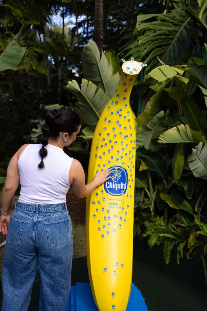 A woman places a sticker on a giant banana at he Chiquita banana stand at Art Basel Miami Beach.