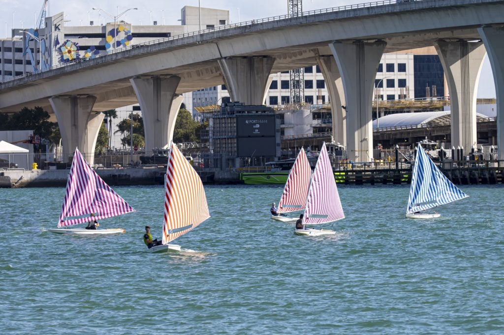 Daniel Buren, Voile/Toile–Toile/Voile (Sail/Canvas–Canvas/Sail). Sunfish sailboats with striped sails race in a regatta on Miami's Biscayne Bay, with a highway overpass in the background. 