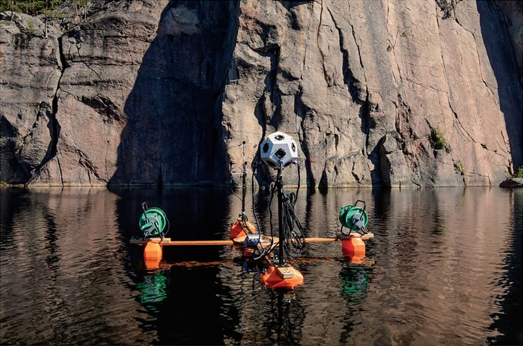 An image of a custom-built raft used for summertime recordings, Olhavanvuori rock art site in the background.