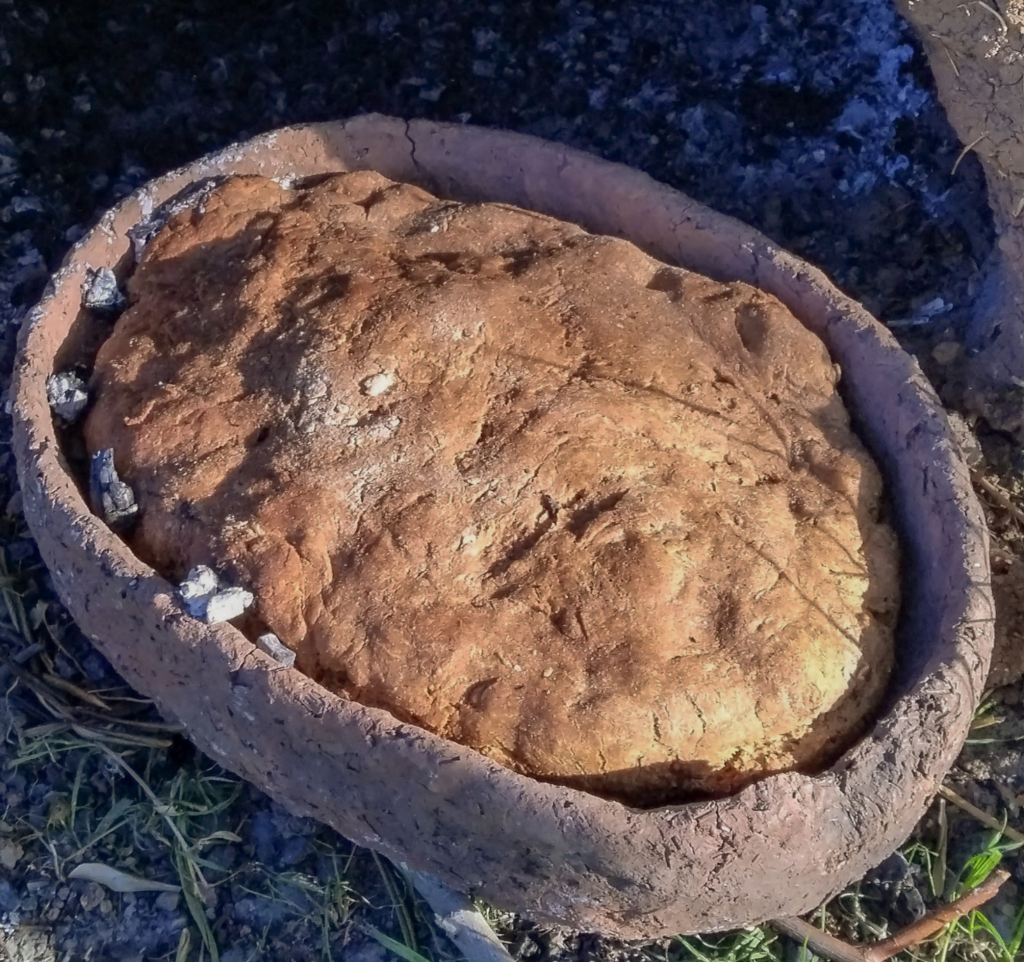 a focaccia bread with a bumpy crunchy golden brown crust in a tray covered with pieces of lard and sprinkled with salt lying on a field of grass