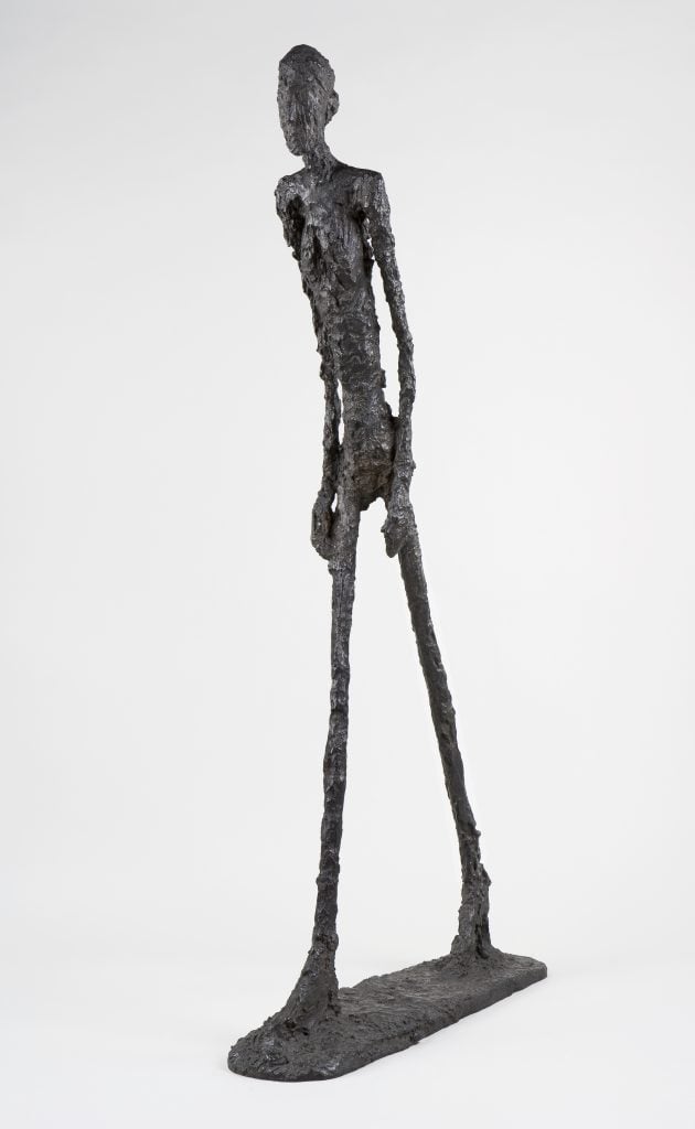 Giacometti's 'Walking Man I' sculpture against a white background.