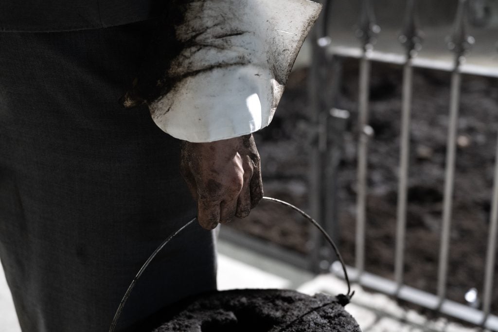 Close-up of a hand gripping a bucket handle, stained with dirt, against an installation backdrop.