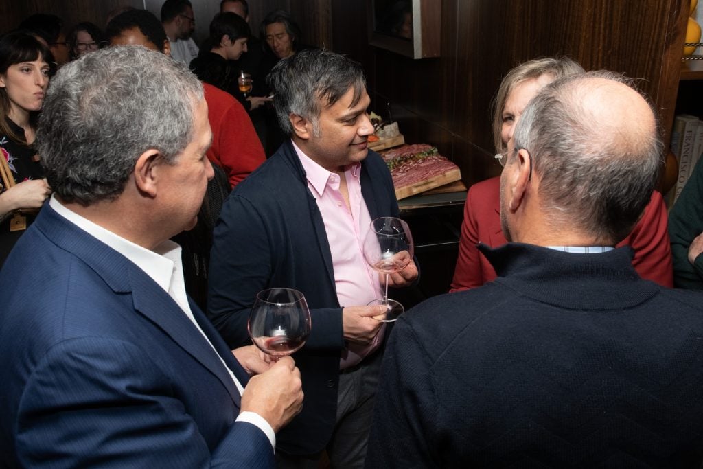 Several people stand around art dealer Kavi Gupta at a wine drinking event